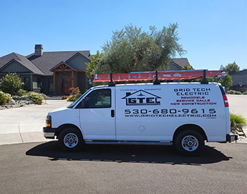 A white van with the words Grid Tech Electric and their logo which is in the shape of a house with the letters GTE.  It also has their phone number which is 530-680-9615. The van is parked in front of a nice house.
